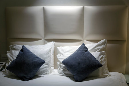 Leather bed, pillows and white cotton bedlinen. Bedroom interior elements. Big luxury comfortable double bed with white and blue linen pillows, blanket. Elegant sleeping room, illuminated at night.の写真素材