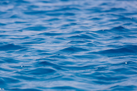 Defocused blurred the motion of blue water surface at the sea, lake. water surface texture. Abstract beautiful ripples, splashes and bubbles. banner background. Water waves in sunlight with copy spaceの写真素材