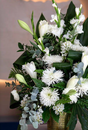 Bouquet of white flowers, chrysanthemums and lilies in glass jar on white table against neutral wall background. Fresh, lush, wedding lily bouquet of colorful flowers, gift on blurred background.の写真素材