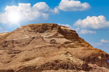 Background of mountains and sun in the blue sky in Dead Sea, Israel. Beautiful desert landscape among the sands and stones. Large stone ridge against the background of a blue sky with white cloudsの写真素材