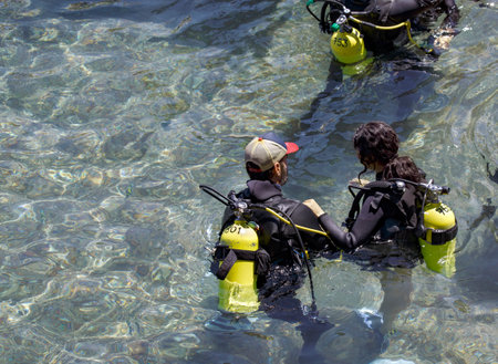 Diving with aqualung lesson in open water. Scuba diver, instructor before diving into deep sea. Waiting on the surface before free diving. Male and women in scuba diving suit is preparing to diveの写真素材