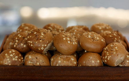 Freshly baked hamburger buns lie with sesame seed on a wooden tray. Brown flavored pastries with white sesame seeds. Fresh homemade bread roll or bun with flax and sunflower seeds in wooden tray.の写真素材
