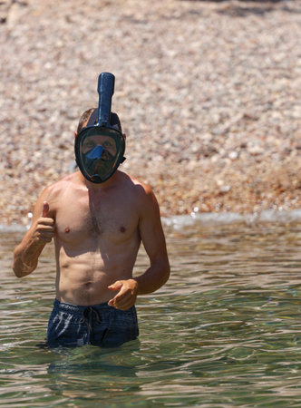 Young man wearing diving face scuba on beach. Shirtless man make thumbs up in sea wear underwater wide view snorkel swimming mask. Snorkel mask let him get more out of their underwater adventures.の写真素材