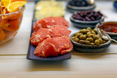 Defocused background of delicious red grapefruit without peel and green olives in a wooden bowl. Selective focus with shallow depth of field. Oranges and Grapefruit for eating. Olives in olive oil.の写真素材