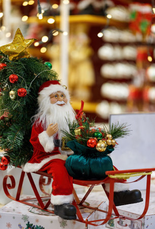 Toy Santa Claus with a beard sitting in sleigh, bokeh background. Christmas sleigh with bag, sledge sack. Xmas Gifts Toys, bright tree toys, present and New Year gifts. Santa's hurries to deliver giftの写真素材