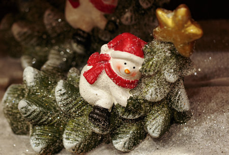 Snowman decorated for christmas. Small snowman figurine on blurred background, happy snowman for winter holidays christmas tree and lights in the background, bokeh, raining light, snow and snowflakesの写真素材