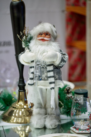 Santa Claus Figurine standing with a gifts bag, christmas tree branch. A miniature little Santa Claus doll holding christmas tree and bell. Ceramic statuette of Santa Claus with a hat on a table.の写真素材