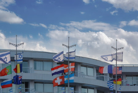 International flags on a modern building under a partly cloudy sky. The flags represent different...