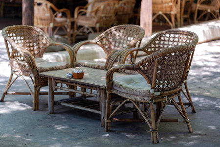 Outdoor setting with three wicker chairs and a matching table adorned with cushions. The furniture is arranged on a concrete floor under the shade, creating an inviting atmosphere for relaxationの写真素材