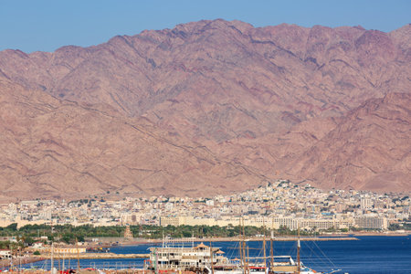 a coastal city nestled at the foot of a massive rugged mountain range in Elam, Israel. The citys architecture is dense with buildings closely packed together. Boats are docked near the shore a portの写真素材