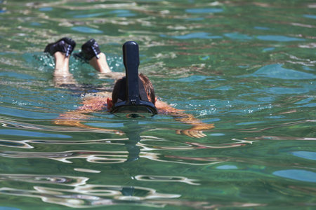 A man of a black snorkel mask swims through clear turquoise water, creating ripples as he moves. The man's strong strokes propel him forward as he enjoys the serene beauty of the sea. Vacationの写真素材