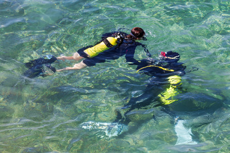 Two scuba divers are seen floating on the surface of sea. They are wearing black wetsuits and have yellow oxygen tanks. Equipped with a snorkel and mask, they are ready for underwater explorationの写真素材