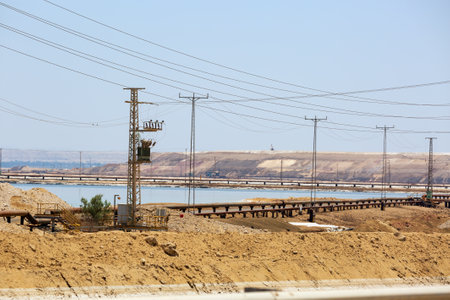 Tranquil afternoon by a serene Dead sea with electrical lines. A peaceful scene unfolds by a calm sea under a clear sky, with utility poles and electrical lines running parallel to the water. Israelの写真素材