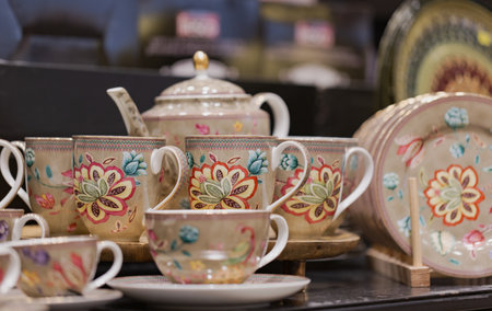 A porcelain tea set with intricate floral designs against a dark background. The set includes cups, saucers, a teapot, and plates. Each piece is adorned with vibrant artwork of flowers and leaves.の写真素材