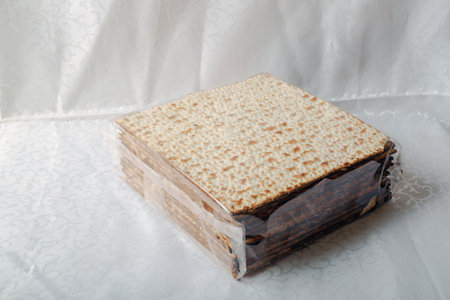 Box covered with matzah, an unleavened flatbread significant in Jewish Passover on a white tablecloth. The surface is perforated and browned, highlighting its baked texture. Matzo bread, unleavenedの写真素材