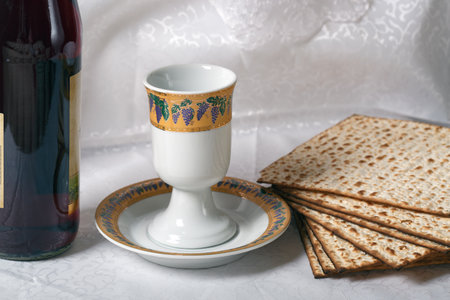 Wine bottle, an ornate goblet, and matzah bread against a white lace backdrop. The matzah is crisp, browned, and patterned with holes. Pesah celebration, Jewish Passover holiday with passover sederの写真素材