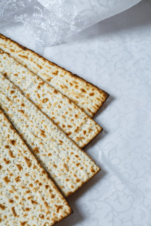 Pieces of matzo, a type of unleavened flatbread integral to Jewish Passover. The matzo is light brown with charred spots indicating its baked nature. The matzah is laid out on a white textured surfaceの写真素材