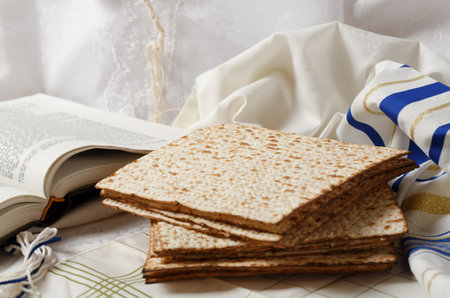 Stack of matzah, a book, and a tallit. The matzo is in the foreground. Adjacent to it lies an open book Tora. The setting appears serene and peaceful, religious traditional Jewish setting passoverの写真素材