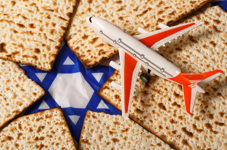 Small toy airplane resting on matzah pieces that are arranged around a blue and white Star of David. The airplane with orange wings and a white body is detailed. The matzah showcases its baked textureの写真素材