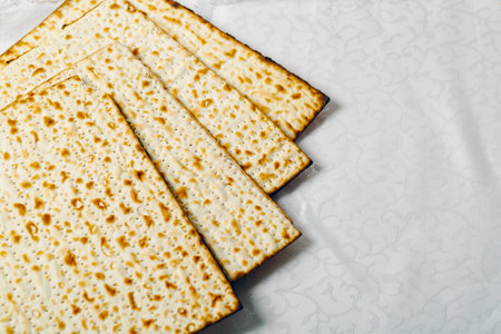 Matzo, an unleavened flatbread integral to Jewish Passover on a textured white surface. The matzo,...
