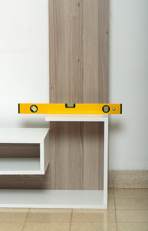 Yellow spirit level on a wooden shelf that is being assembled. The shelf is against a white wall and the floor is beige. The level indicates that the horizontal piece of the shelf is perfectly alignedの写真素材