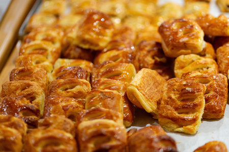 Freshly baked golden brown pastries with sweet or savory ingredients on display at a local bakery. An assortment of pastries, with a glossy and flaky texture, is neatly arranged on parchment paper.の写真素材