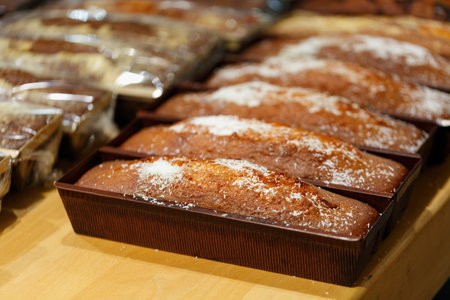 Freshly baked and neatly aligned loaves of sweet cupcakes rest on a wooden counter, ready for customers at a local bakery during the morning hours. Sweet cupcakes sprinkled with coconut shavings.の写真素材
