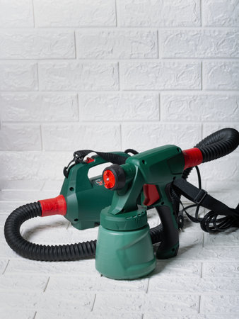 Green and red electric paint sprayer on white brick background in daylight. An electric paint sprayer with green and red parts is placed on brick surface showing its design and functionalityの写真素材