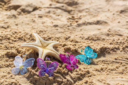 Starfish with a colorful artificial butterflies on beach sand. A starfish and colorful butterflies on a sandy beach. Suggests a creative or decorative theme, possibly for an event or artistic conceptの写真素材