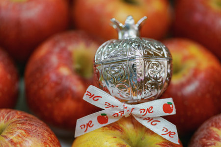 Decorative silver pomegranate with intricate designs, placed among real apples. The pomegranate has a ribbon with the Hebrew inscription words shana tova is attached to it which means Happy New Yearの写真素材