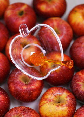 Red apples with a clear apple shaped plastic container placed on top of them. The container has a honey dipper inside it, suggesting the theme of Rosh Hashanah Jewish New Year holiday concept. Israelの写真素材