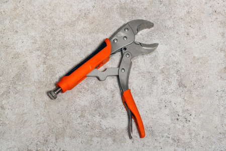 A single orange and gray slip joint plier lying on a textured floor tiles. This tool is commonly...