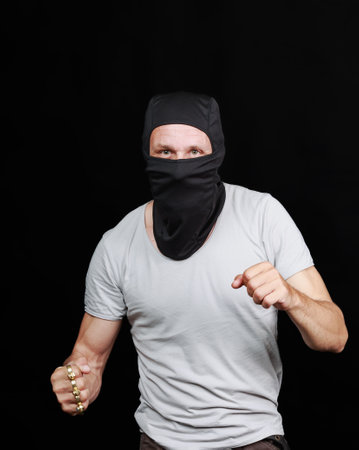Man wearing t-shirt and a black balaclava mask. Male is posed as if they are delivering a punch with one arm extended forward and the other bent at the elbow on black backgroundの写真素材