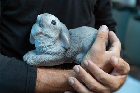 Hands holding a toy bunny statue. Beautifully crafted stone rabbit figurine. Garden features fine playful pose. Garden figure animal. Easter bunny decoration for gardenの写真素材
