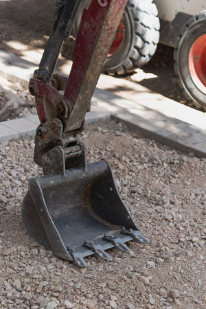 Bucket and the wheels of a compact loader at a construction site with gravel and paving stones in...