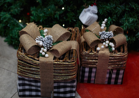 Two decorative holiday gift boxes are displayed under a Christmas tree, adorned with rustic bows,...