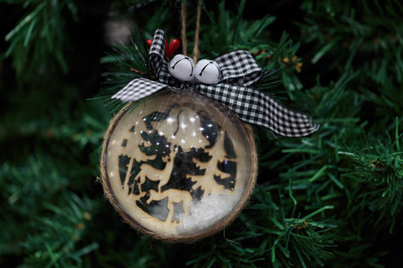 A uniquely wooden ornament captures a winter woodland scene with deer and trees, carefully placed on a decorated holiday tree. The addition of a black and white checked ribbon enhances its charm.の写真素材