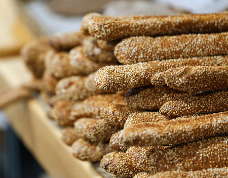 Stacks of golden brown sesame breadsticks are prominently displayed on a wooden table. Freshly baked sesame breadsticks arranged neatly on display. Fresh Italian grissini breadsticks with sesame seedsの写真素材