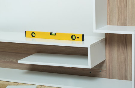 A yellow spirit level is placed on wood shelf during the installation process, ensuring precise...