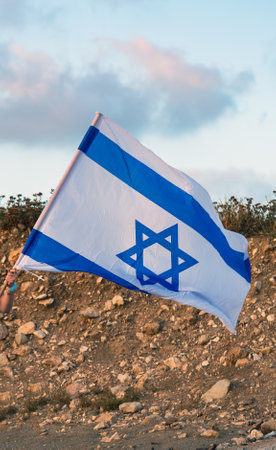 A woman hand waving big Israeli national flag against blue sky. Memorial day Yom Hazikaron, Israel...