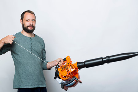 A man operating Engine pull cord a Air Blower Tool. Starting a handheld leaf blower, cordless, electric leaf blower isolated on gray background. Garden and lawn care concept. Studio shotの写真素材