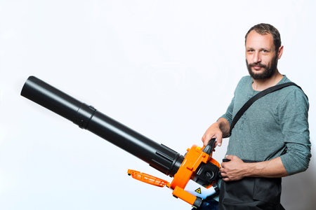 Handsome bearded man holding a Garden blower with a collection bag on gray background. Worker with a leaf blower with a bag. Leaf blower with dust filter bag. Handheld Blowing leaves away. Toolsの写真素材