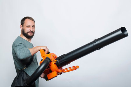 Bearded man holding a Garden blower with a collection bag on gray background. Worker with a leaf blower with a bag. Leaf blower with dust filter bag. Handheld Blowing leaves away. Toolsの写真素材