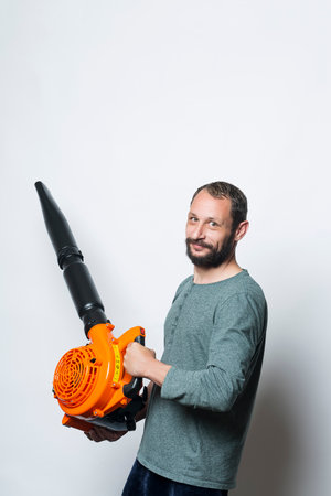 The worker holds a blower in his hands, isolated on white. Man on a studio with a leaf blower. Landscaper operating gas Leaf Blower. Tools. Gardening. Machine. Orange blower machine with black tubeの写真素材