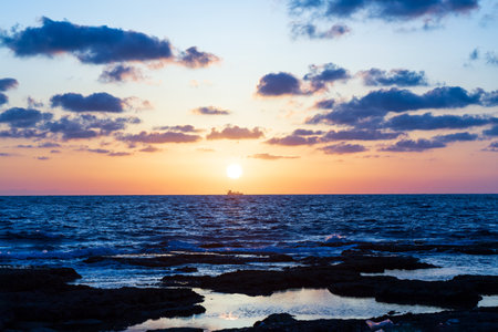 The Mediterranean sea glows under a golden sunset, with shimmering waves reflecting the fiery hues of the sky. A tranquil beauty envelopes the coast as day fades into night in cityの写真素材