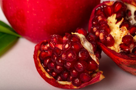 Ripe pomegranate fruit with green leaves on pink backgroundの写真素材