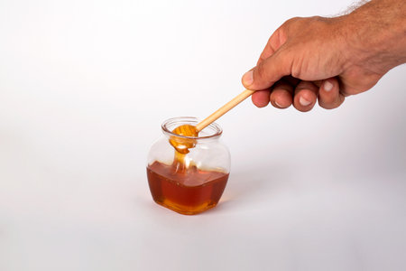Honey dripping from a wooden honey dipper into a glass jarの写真素材