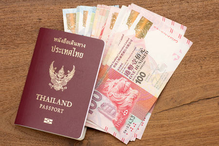 Thailand passport with hongkong currency. brown passport with world currency on teak wood texture tableの写真素材