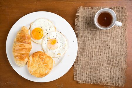 breakfast biscuit croissant egg coffee on teak table top view