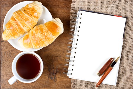 croissant cup coffee white book pen  on teak wood table top viewの写真素材